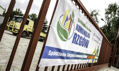 Zdjęcie przedstawia bramę wjazdową. Na niej widnieje duży baner reklamowy, promujący Spółdzielnię Socjalną Komunalka Rzgów